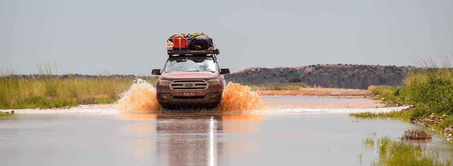 Ford Everest with a loaded Tradesman Oval Alloy roof rack wading trough water over the road near Birdsville in outback Australia.